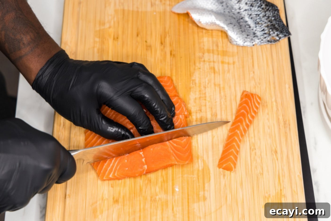 Salmon Morsels 6 Slicing a salmon fillet into uniform strips on a cutting board before cubing.