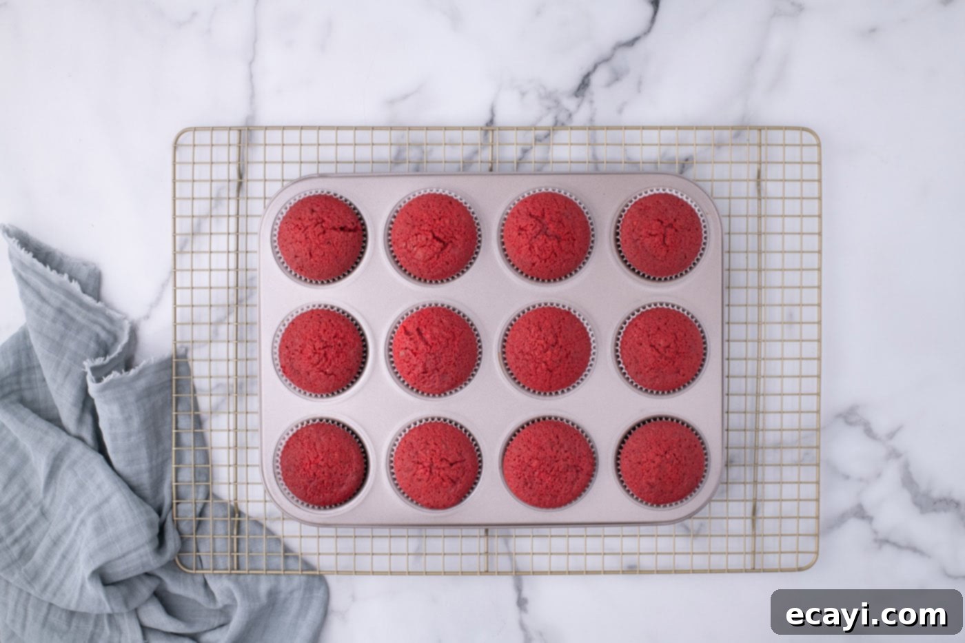 Decadent Red Velvet Treats 14 Freshly baked red velvet cupcakes cooling in a cupcake tin on a wire rack, with some already removed.