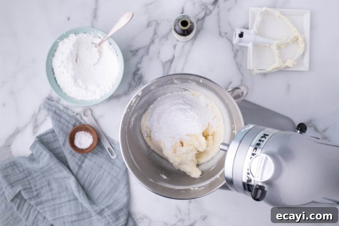 Decadent Red Velvet Treats 17 Gradually adding powdered sugar to cream cheese frosting in a mixer bowl, ensuring a smooth and lump-free consistency.