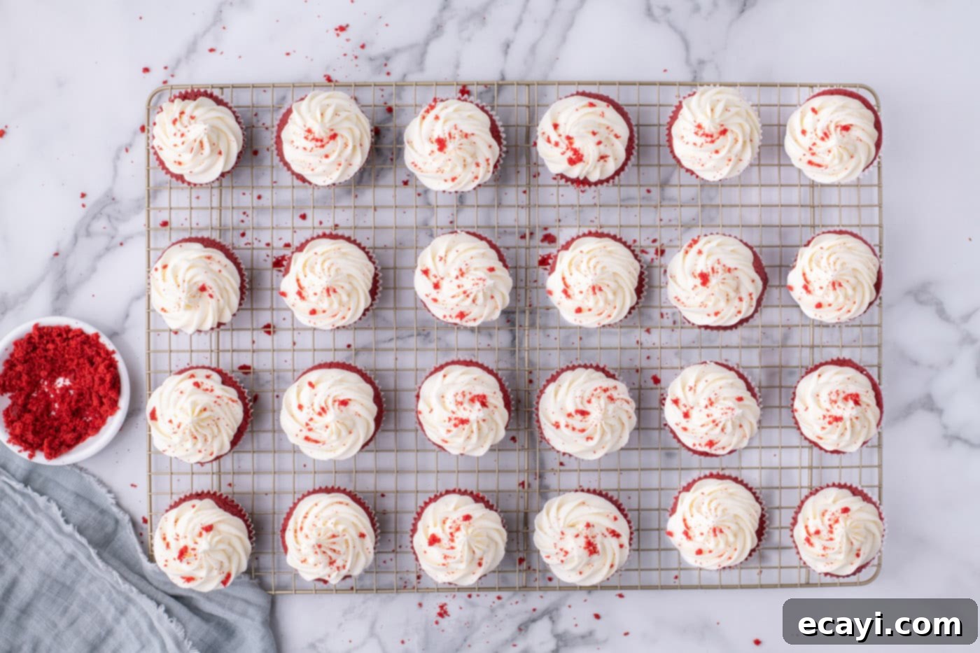 Decadent Red Velvet Treats 18 An overhead shot of exquisitely frosted red velvet cupcakes on a wire cooling rack, garnished with cake crumbs.