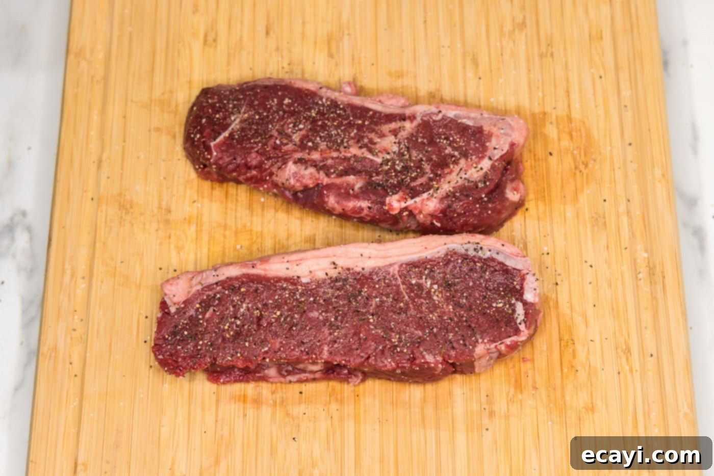 Perfect Sous Vide Steak 5 Seasoned New York strip steaks with garlic salt and pepper on a cutting board, ready for sous vide.