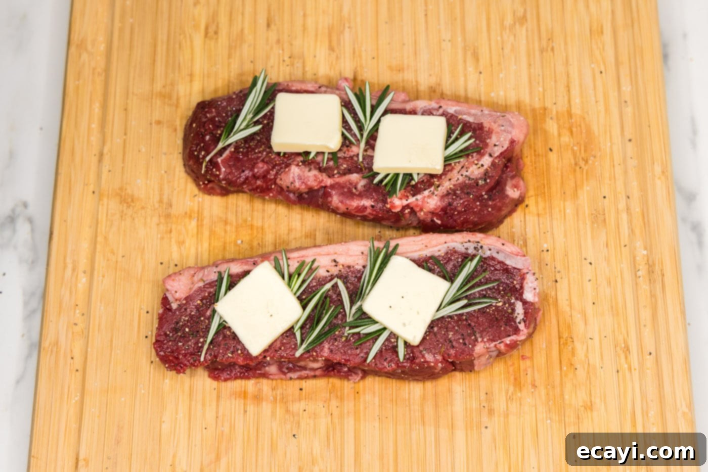 Perfect Sous Vide Steak 6 New York strip steaks topped with fresh rosemary sprigs and pats of butter, ready for vacuum sealing.