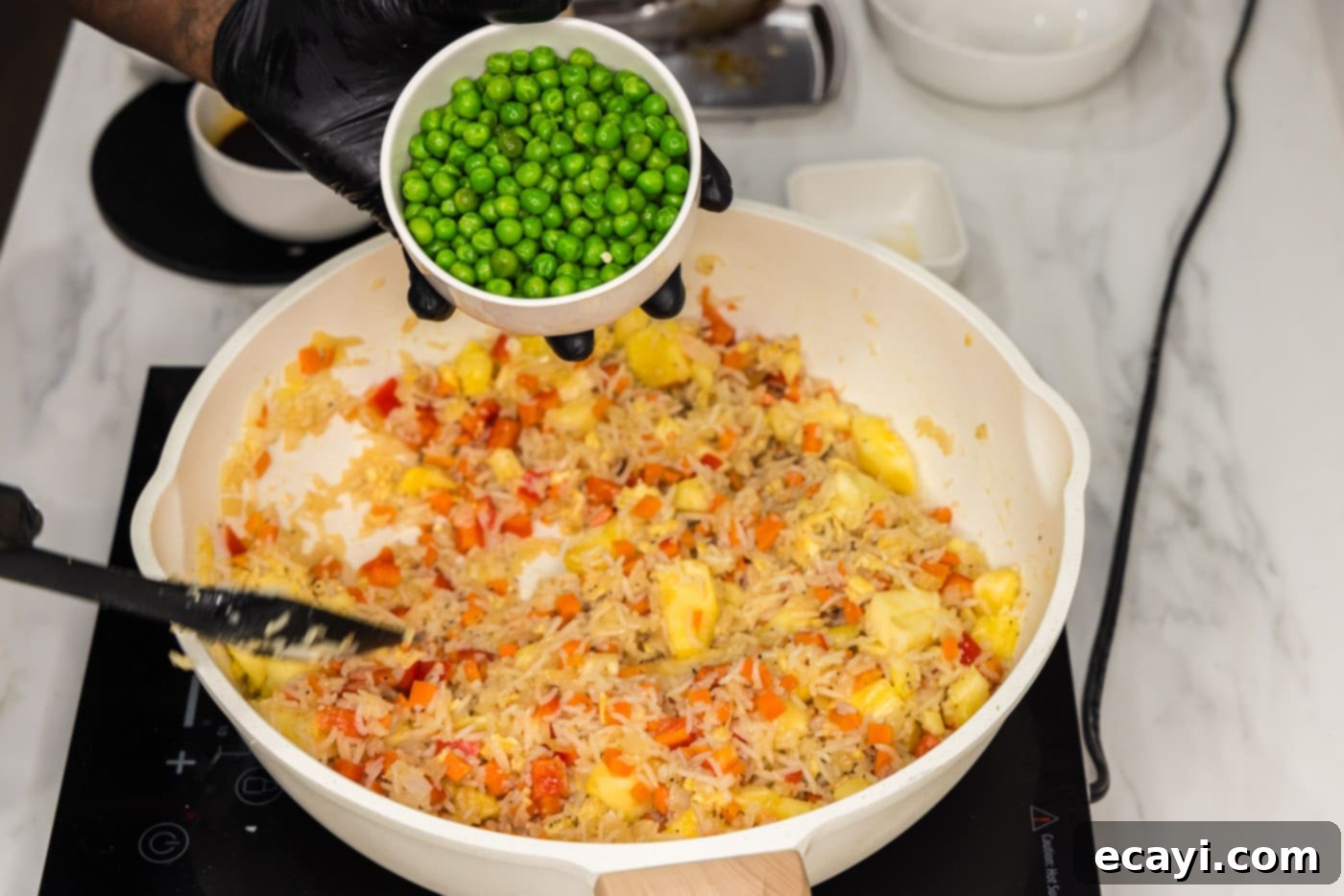 Sun-Kissed Pineapple Rice 12 Frozen peas being added to the skillet of pineapple fried rice, enhancing the dish with vibrant color and a touch of freshness.