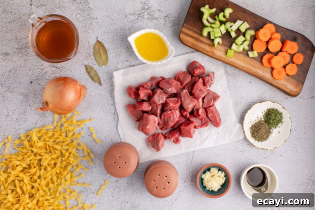 Hearty Beef Noodle Bowl 4 All raw ingredients laid out for making beef noodle soup: beef stew meat, carrots, celery, onion, garlic, egg noodles, beef broth, olive oil, and various seasonings.