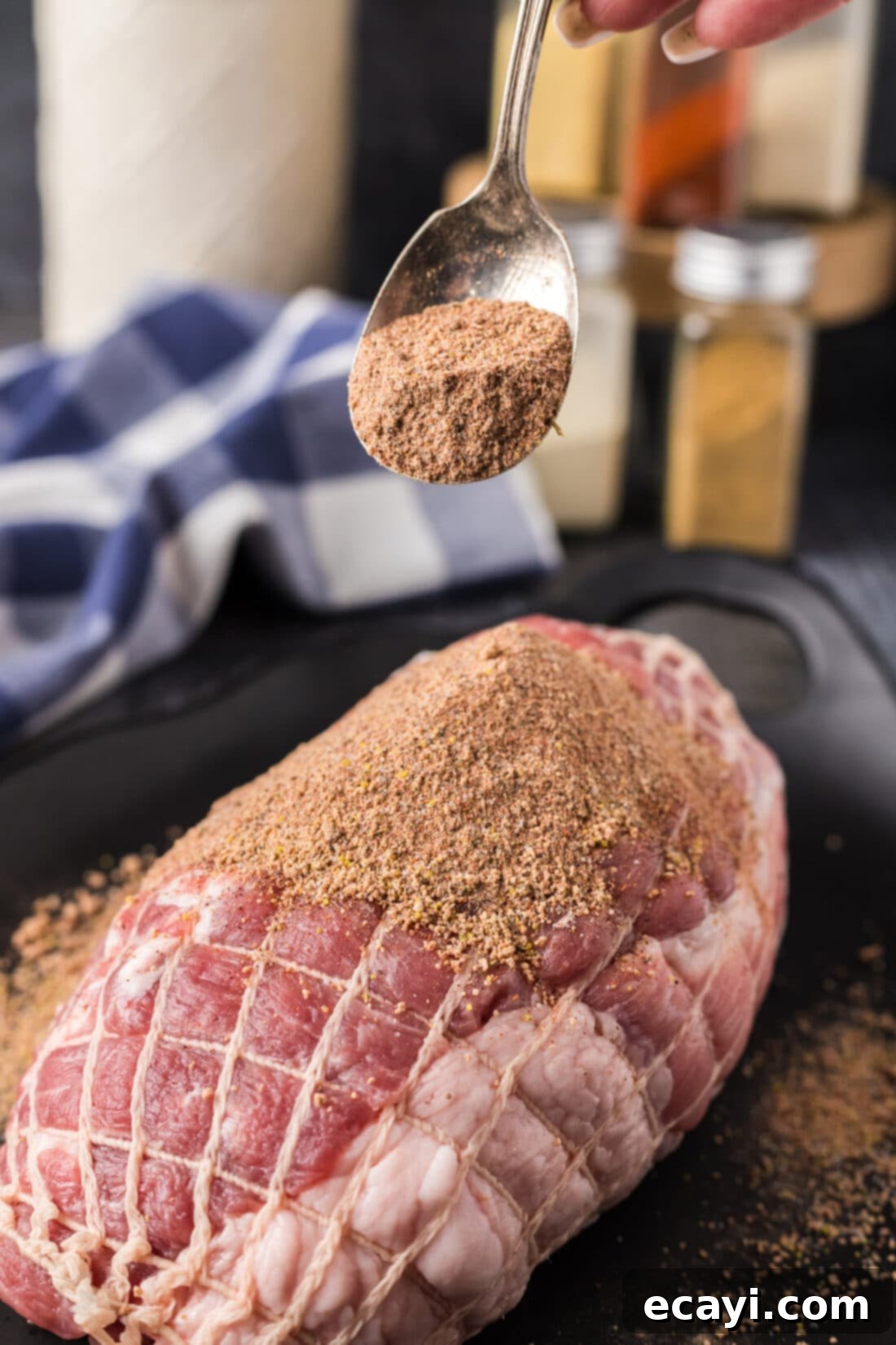Signature Pulled Pork Blend 2 A spoonful of vibrant, homemade pulled pork rub held above a glistening boneless pork shoulder, ready for seasoning.