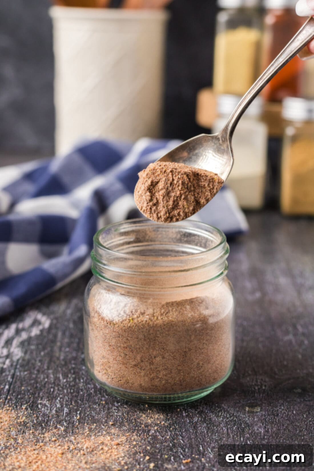 Signature Pulled Pork Blend 3 A spoonful of freshly mixed pulled pork rub poised above a clear seasoning jar, filled with the homemade blend.