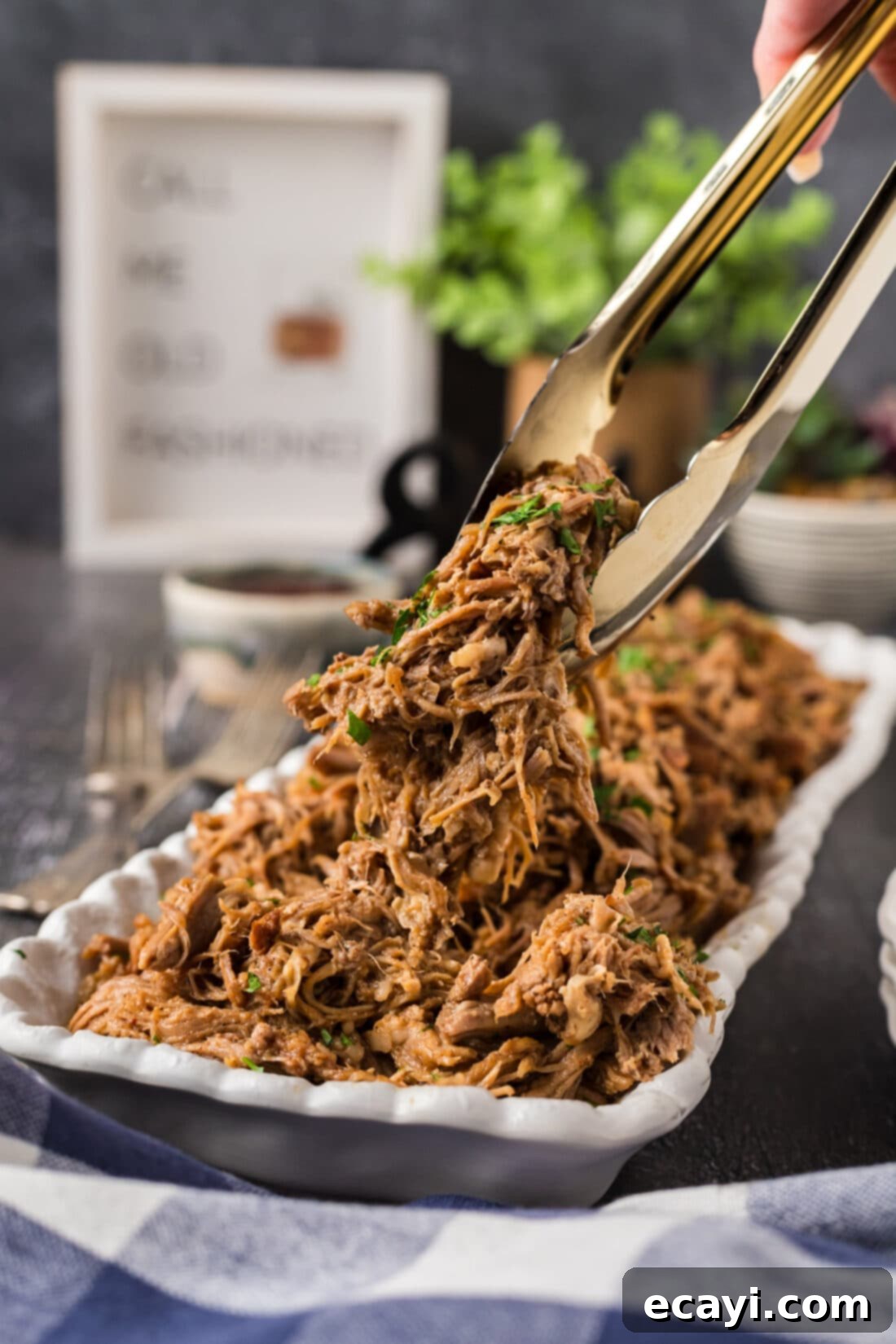 Slow-Cooked Shredded Pork 3 Tongs holding up pulled pork above a platter