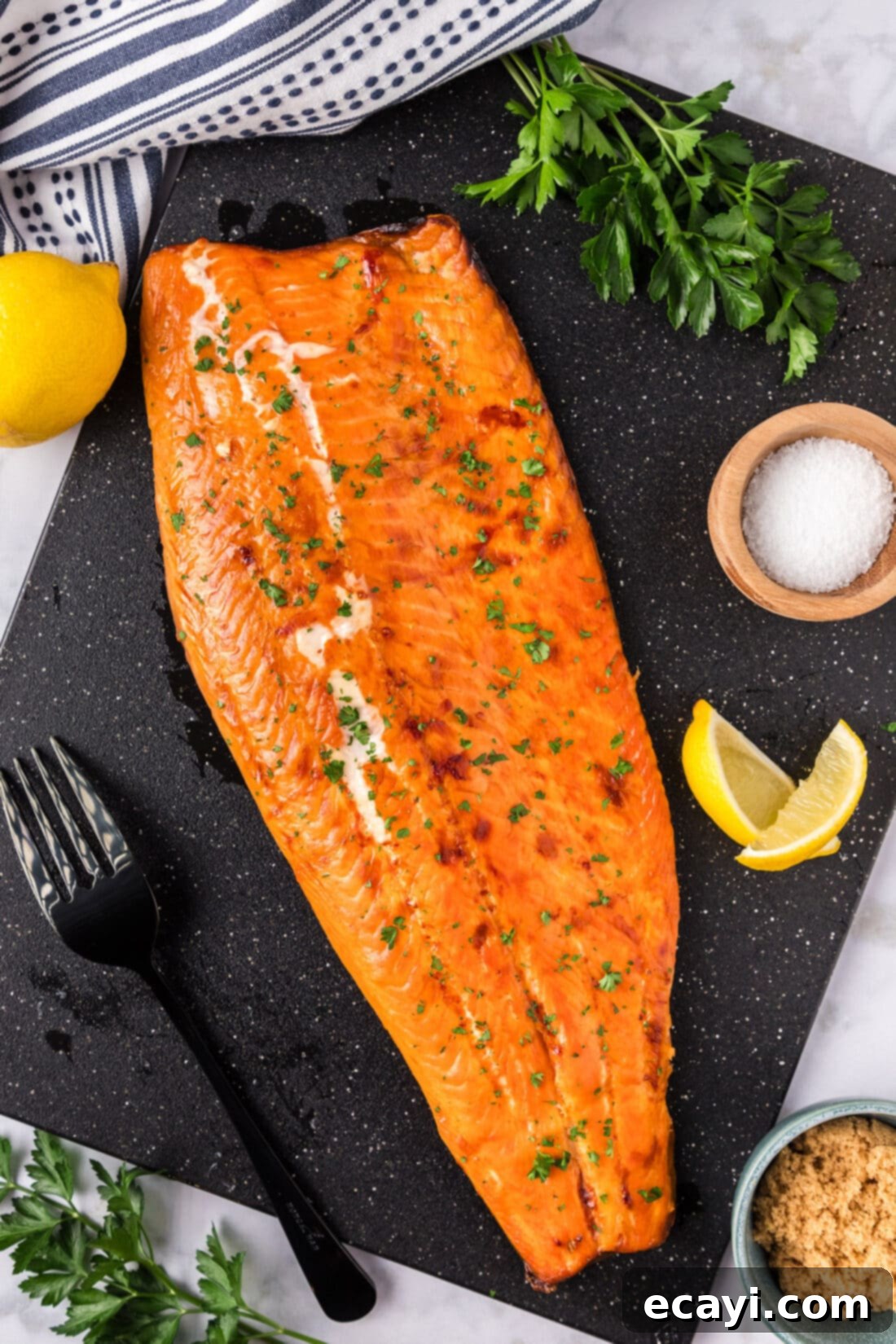 Artisan Smoked Trout 9 Overhead photo of Smoked Trout on a black board, garnished with fresh herbs and lemon wedges.