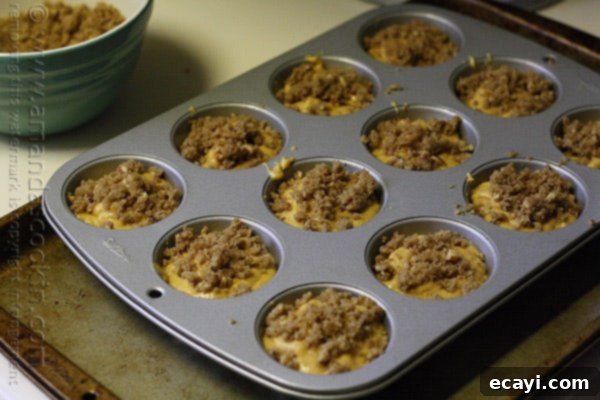 Cozy Pumpkin Mini Cakes with Cinnamon Streusel 15 A close up photo of a muffin tin filled with pumpkin mini cake batter and cinnamon streusel topping.