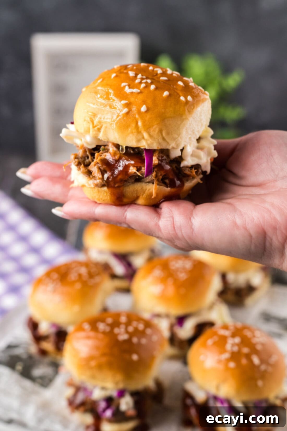 BBQ Pulled Pork Bites 2 Hand holding up a Pulled Pork Slider over more Pulled Pork Sliders, highlighting the tender pork and fresh toppings, perfect for party food