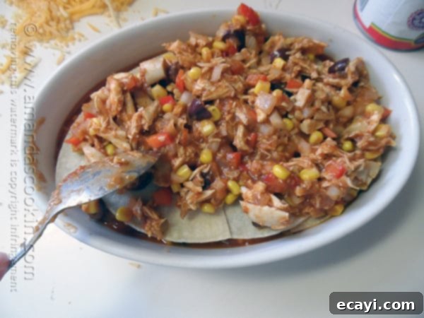 Golden Chicken Tostada Bake 5 Spreading the flavorful chicken mixture evenly over the tortilla layer in the tostada casserole, ready for the next delicious addition.