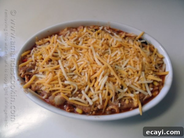 Golden Chicken Tostada Bake 7 The final layer of shredded cheese generously topping the chicken tostada casserole, poised to melt into golden, bubbly perfection in the oven.