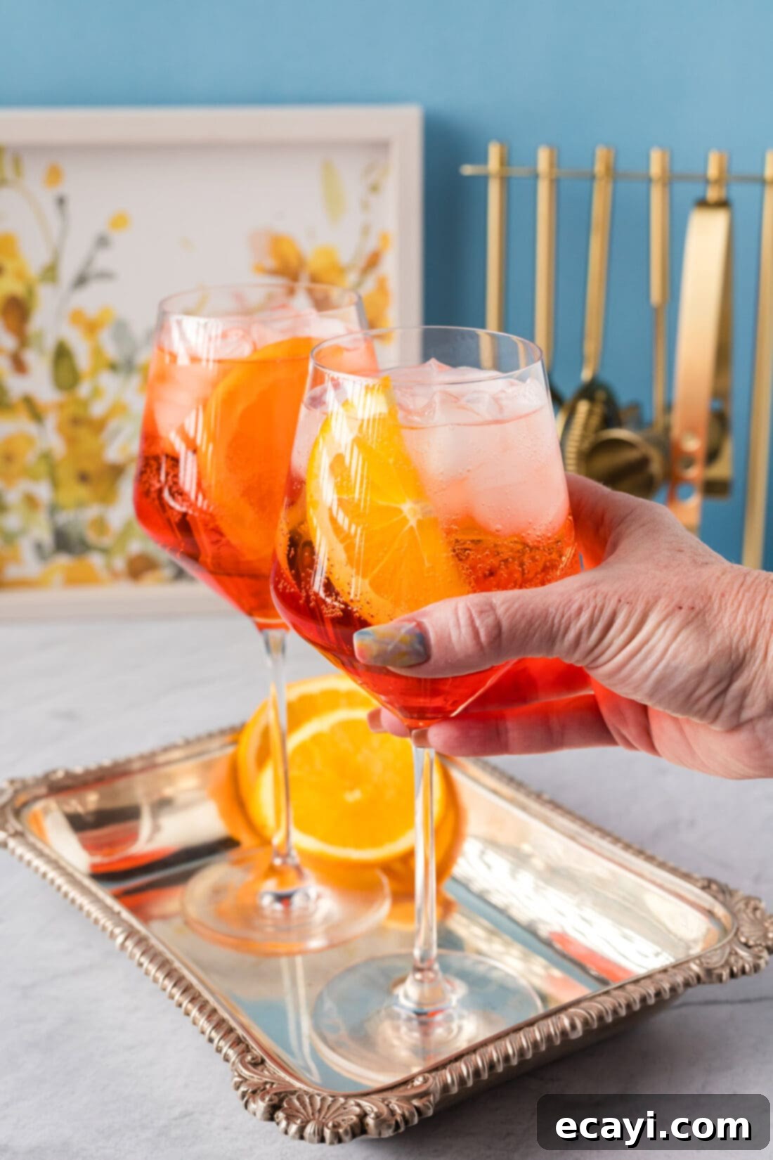 Golden Hour Aperol Spritz 3 A hand gently grabbing a glass of Aperol Spritz, showcasing its vibrant orange color.