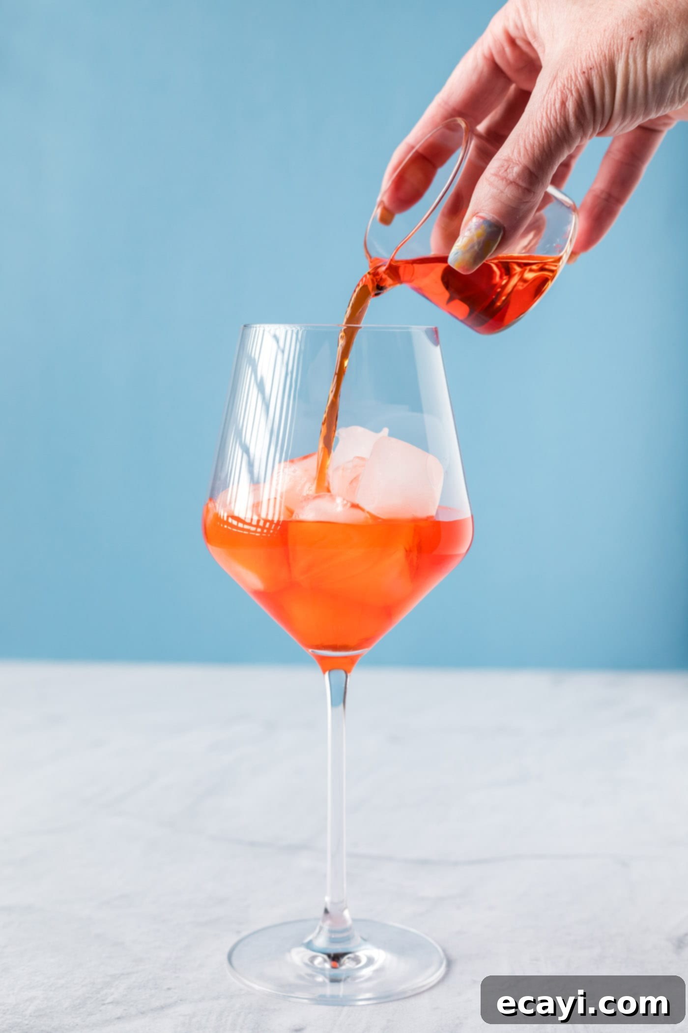 Golden Hour Aperol Spritz 5 Pouring Aperol into a wine glass filled with ice, illustrating the first step of making an Aperol Spritz.