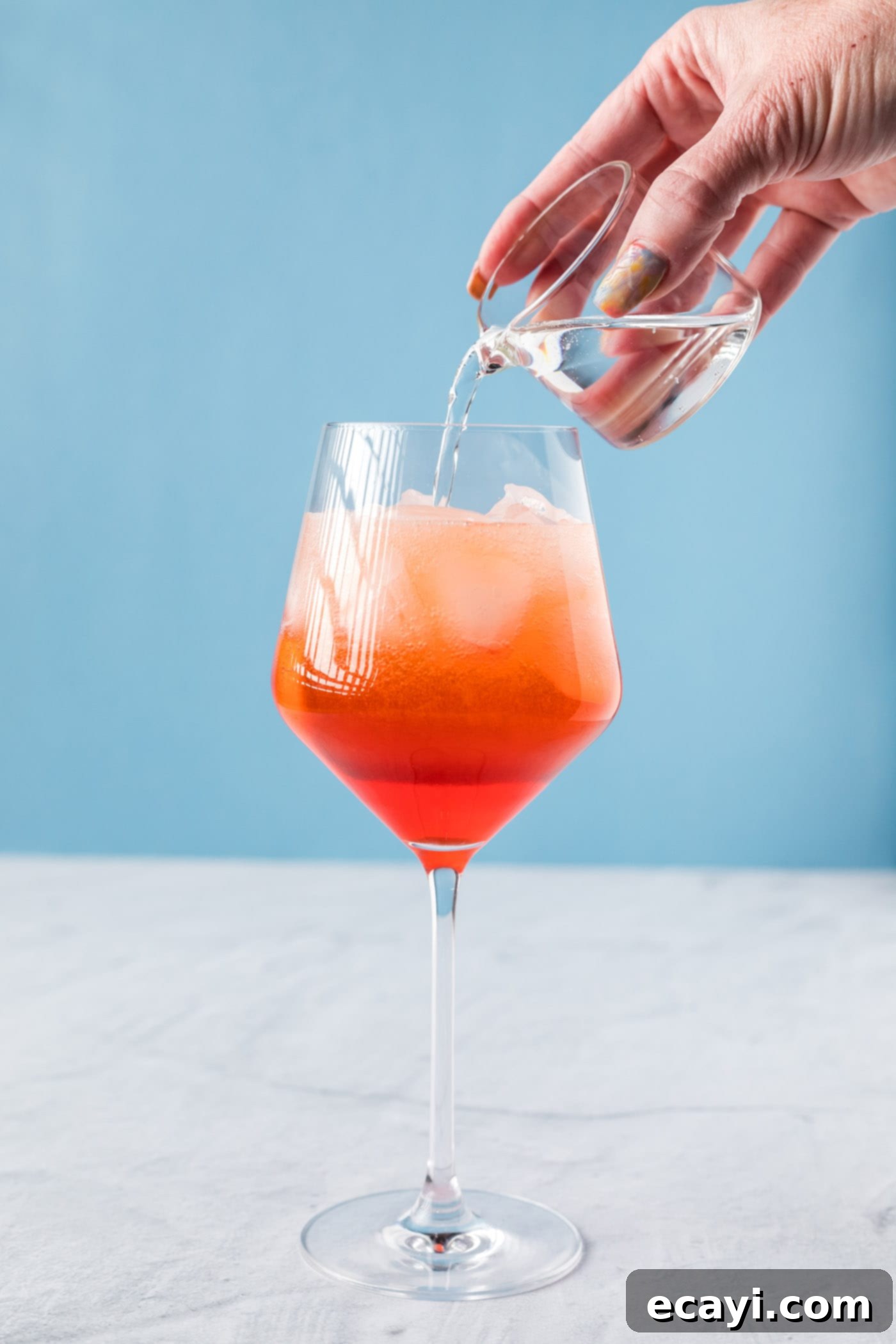 Golden Hour Aperol Spritz 6 Pouring club soda into an Aperol Spritz, showing the final liquid component being added.