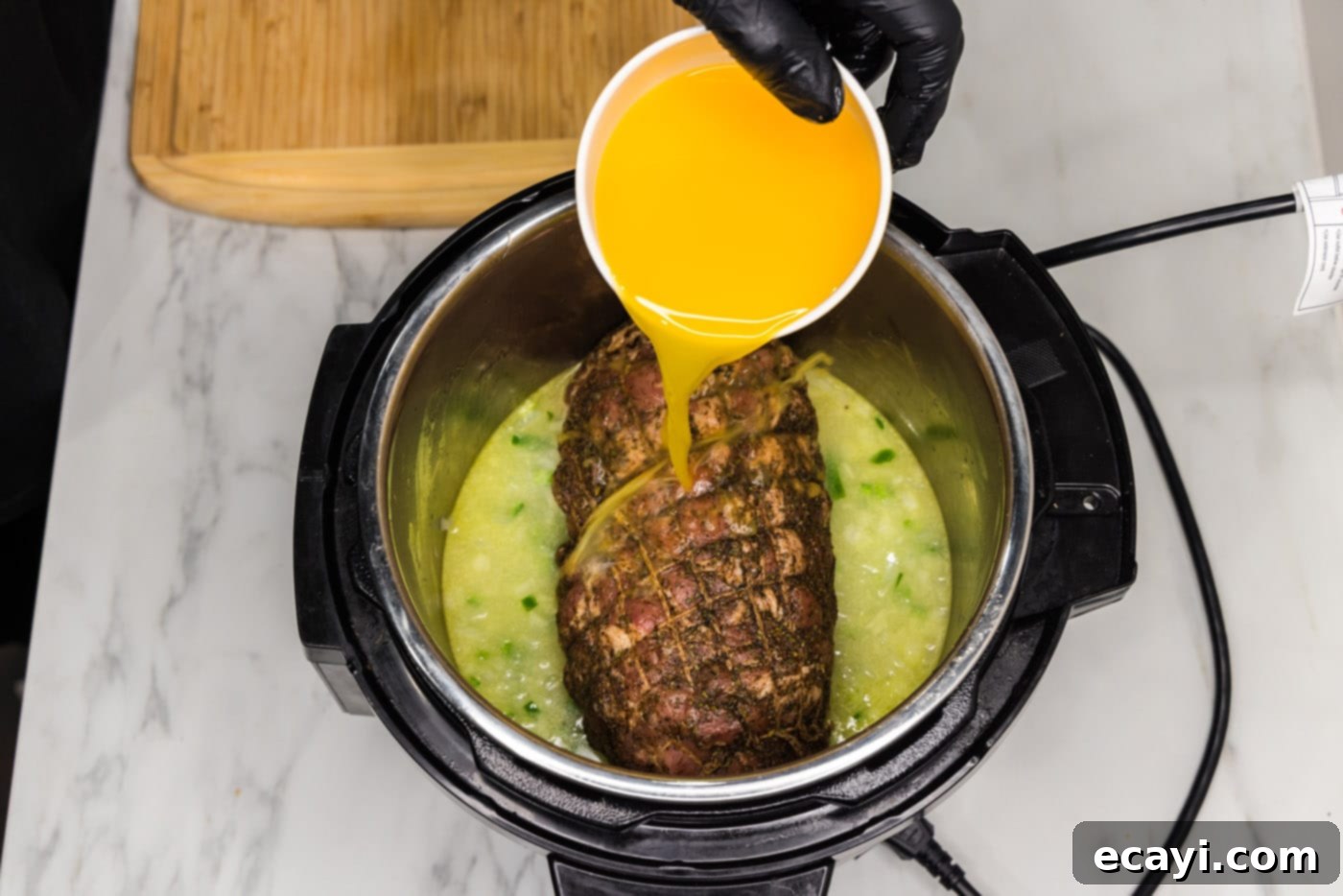 Crispy Instant Pot Carnitas 12 pouring orange juice into instant pot with jalapeno, onion, and pork roast