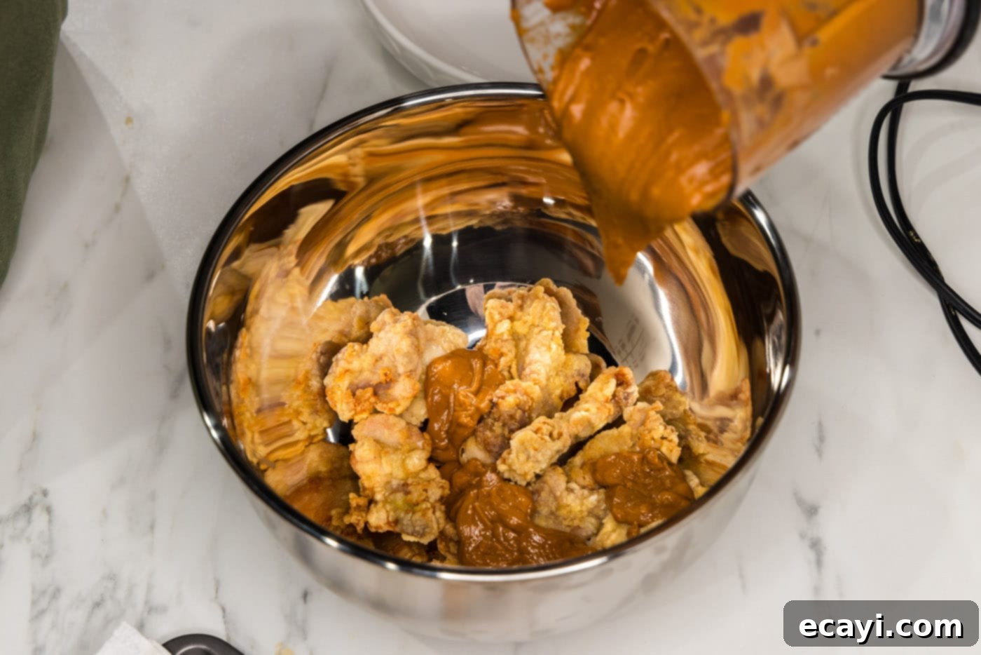 Creamy Peanut Butter Chicken 13 pouring rich peanut butter sauce over fried chicken pieces in a large mixing bowl