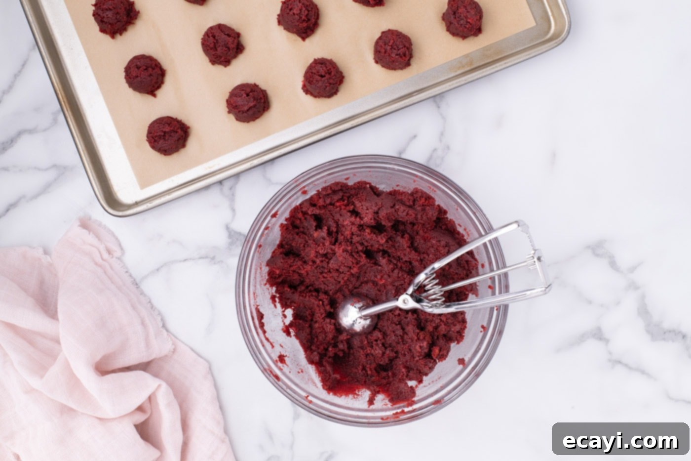 Red Velvet Truffles 11 A small cookie dough scoop resting in a bowl of red velvet cake and frosting mixture, with a portion scooped out.