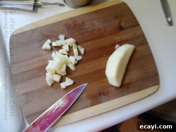 Classic Merryfield Apple Cake 7 An overhead shot of a person chopping fresh apples on a rustic wooden cutting board, ready for the Merryfield apple cake recipe.