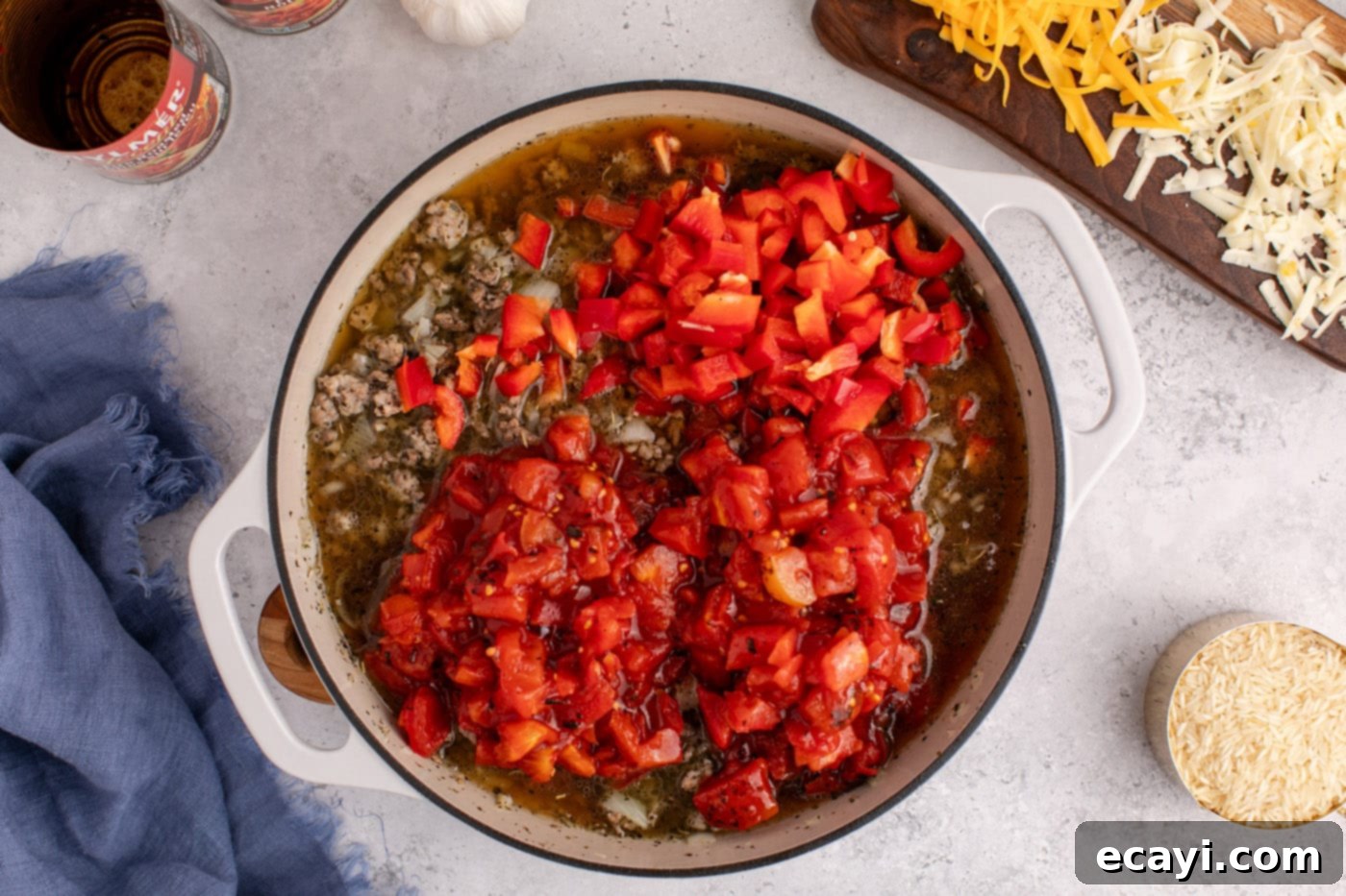 Deconstructed Stuffed Pepper Bake 7 Fire-roasted tomatoes and chopped bell peppers added to the beef and sausage mixture in a skillet, simmering.