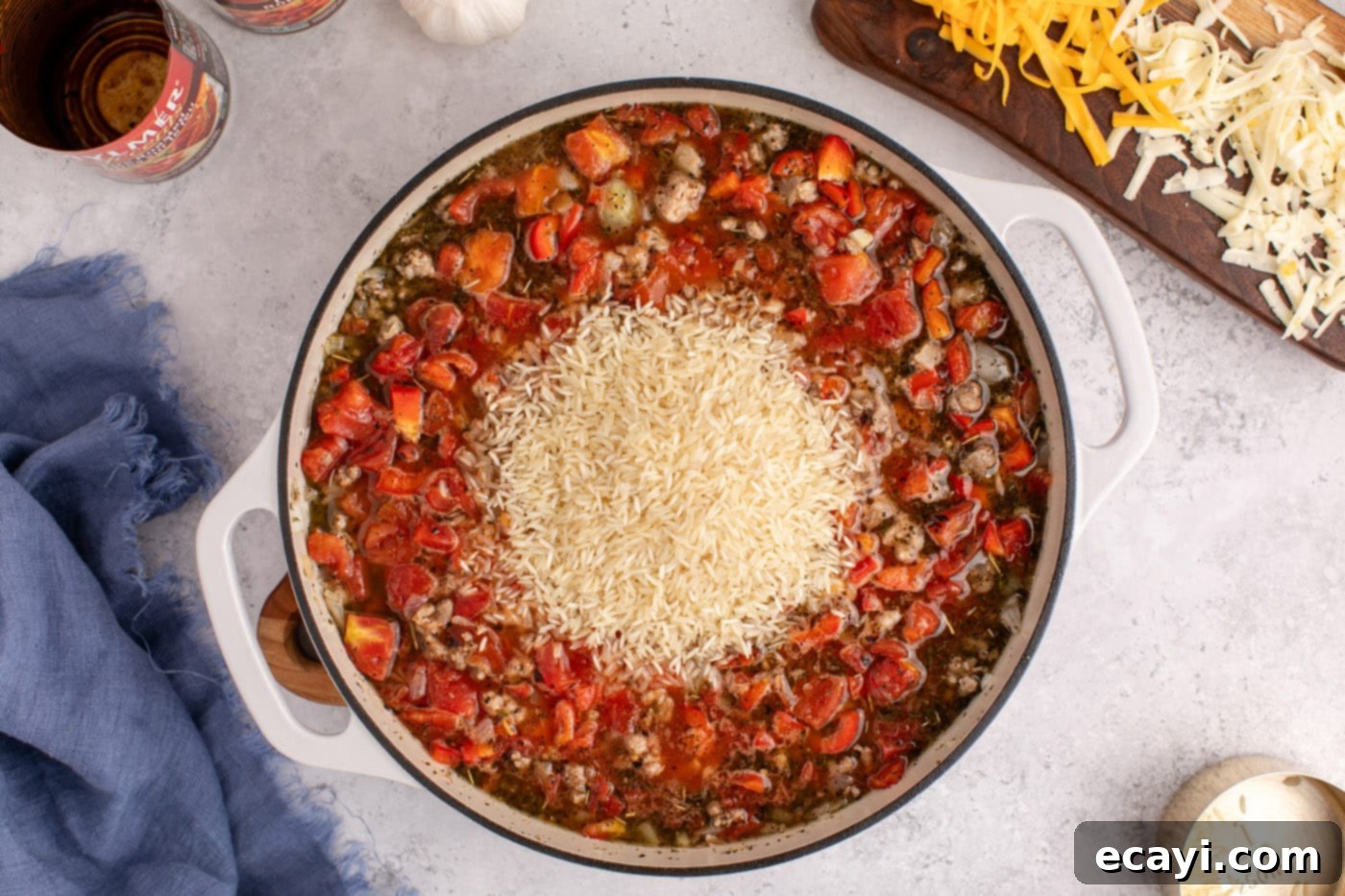 Deconstructed Stuffed Pepper Bake 8 White rice being stirred into the ground beef, sausage, and tomato mixture in a Dutch oven.
