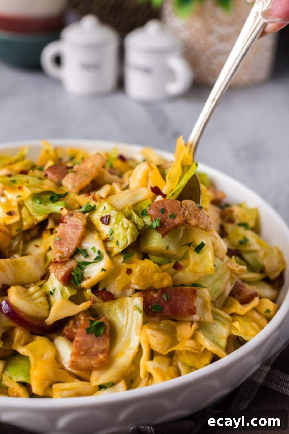 Sizzling Spicy Cabbage 2 A spoon digging into a bowl of vibrant, spicy fried cabbage with visible pieces of crispy bacon and red onion, steam gently rising.