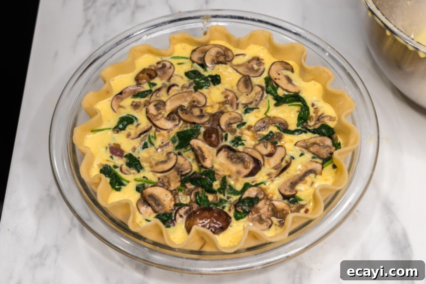 Savory Spinach Mushroom Quiche 13 Final layer of spinach and mushrooms scattered over the egg filling in the pie plate, ready for baking.