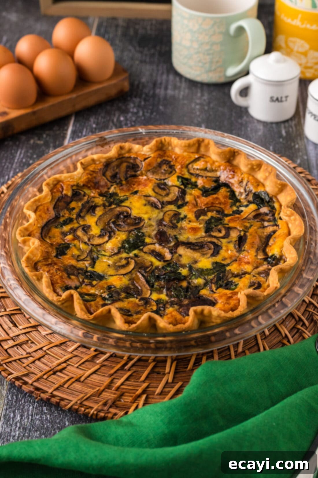 Savory Spinach Mushroom Quiche 3 A whole Spinach Mushroom Quiche resting on a rustic wooden charger, ready to be sliced and served.