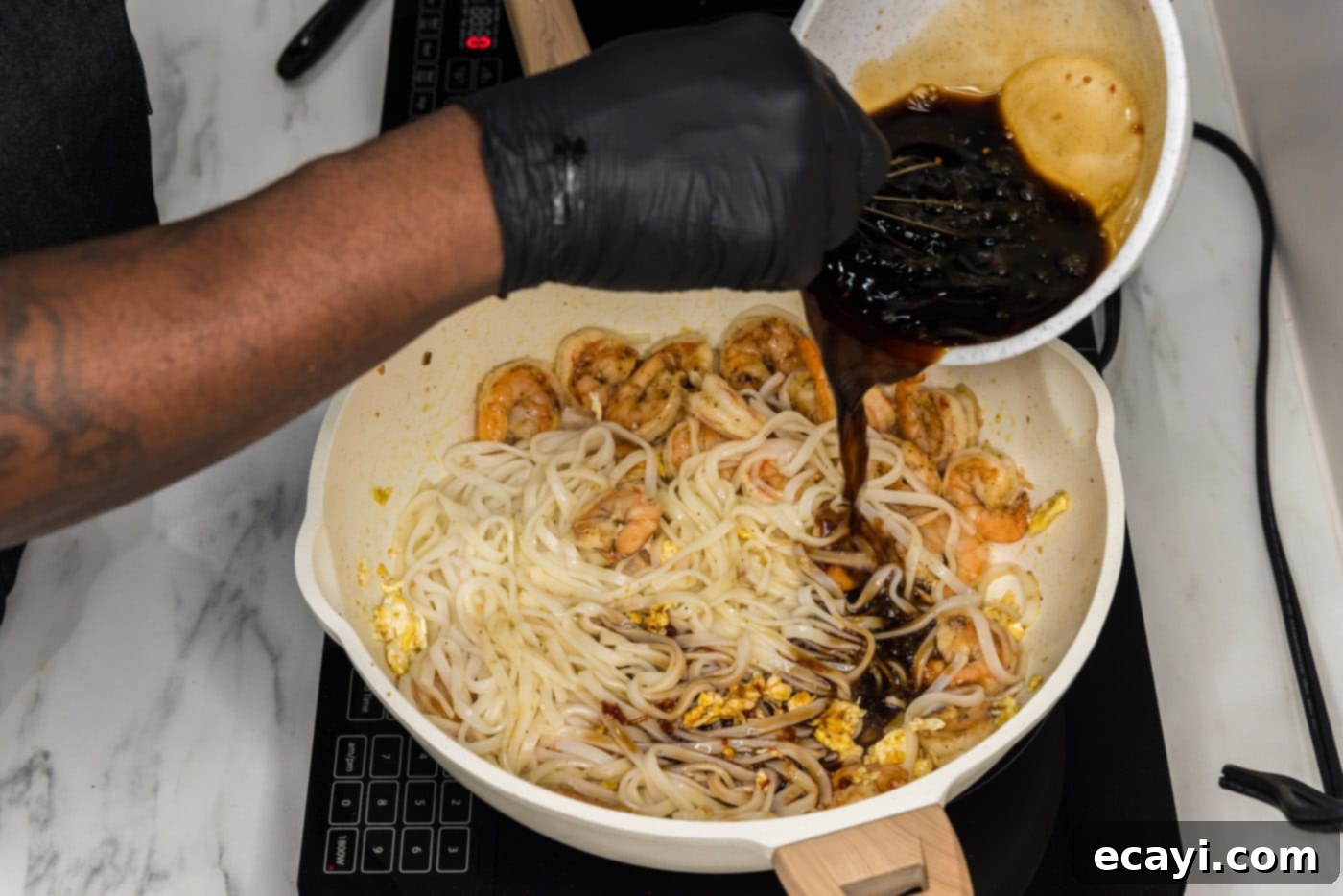 Authentic Shrimp Pad Thai 10 Pouring homemade Pad Thai sauce into a skillet with rice noodles and shrimp