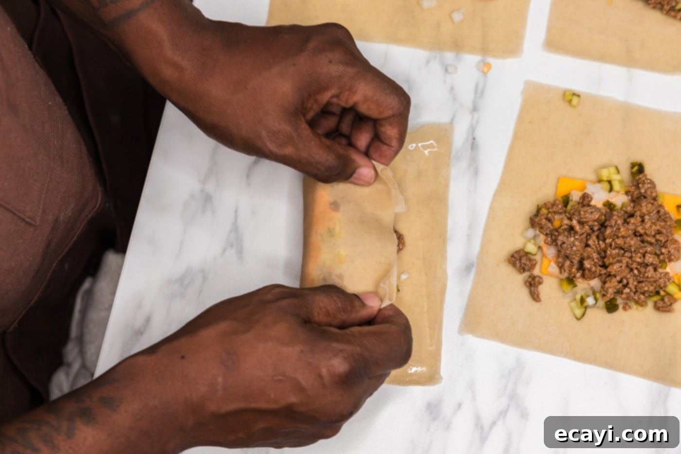 Ultimate Big Mac Egg Rolls 12 hands demonstrating how to fold and roll an egg roll wrapper