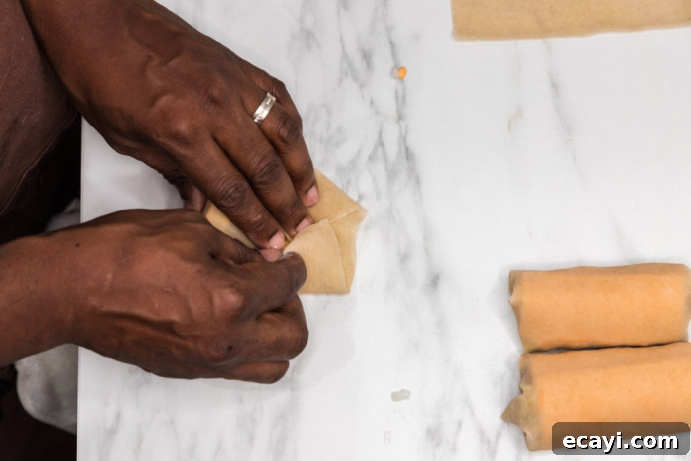 Ultimate Big Mac Egg Rolls 13 hands completing the rolling of an egg roll wrapper, showing a securely sealed egg roll