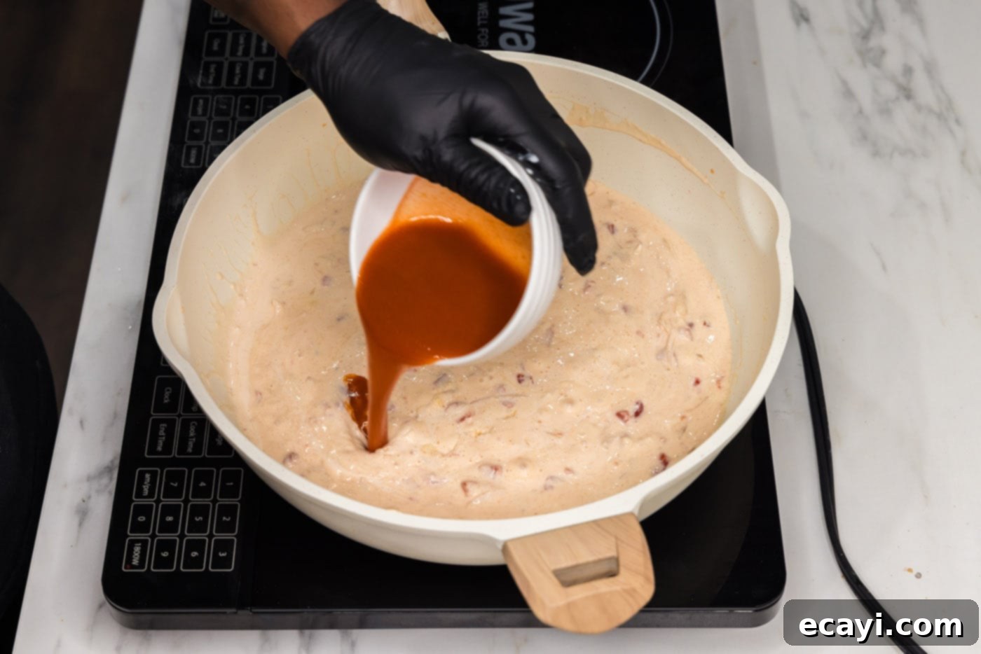 Zesty Buffalo Chicken Pasta 9 pouring hot sauce into skillet with cream cheese mixture