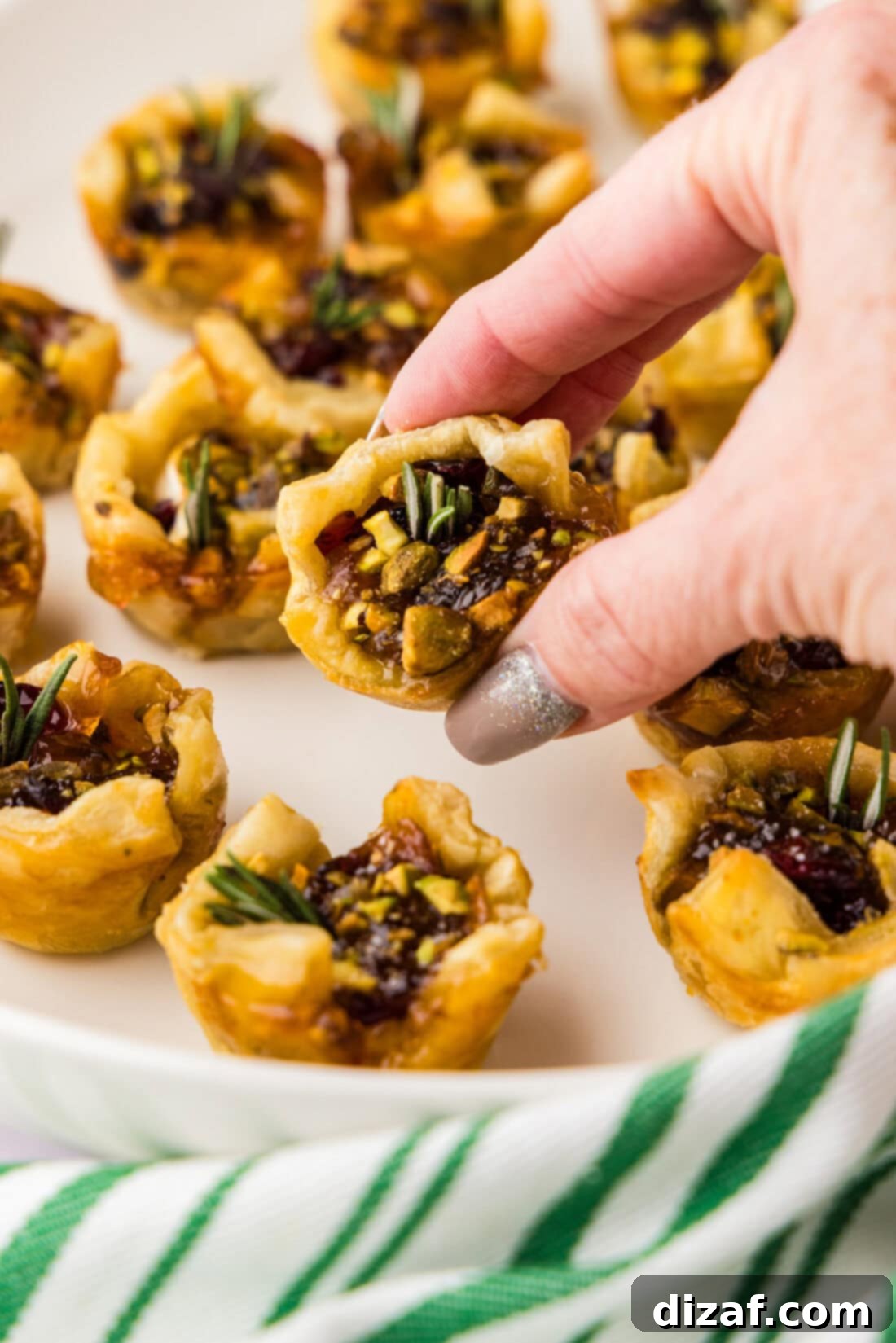 Brie Delights 48 A hand holds a perfectly baked Brie Bite, showcasing its golden puff pastry, melted brie, and vibrant apricot jam.