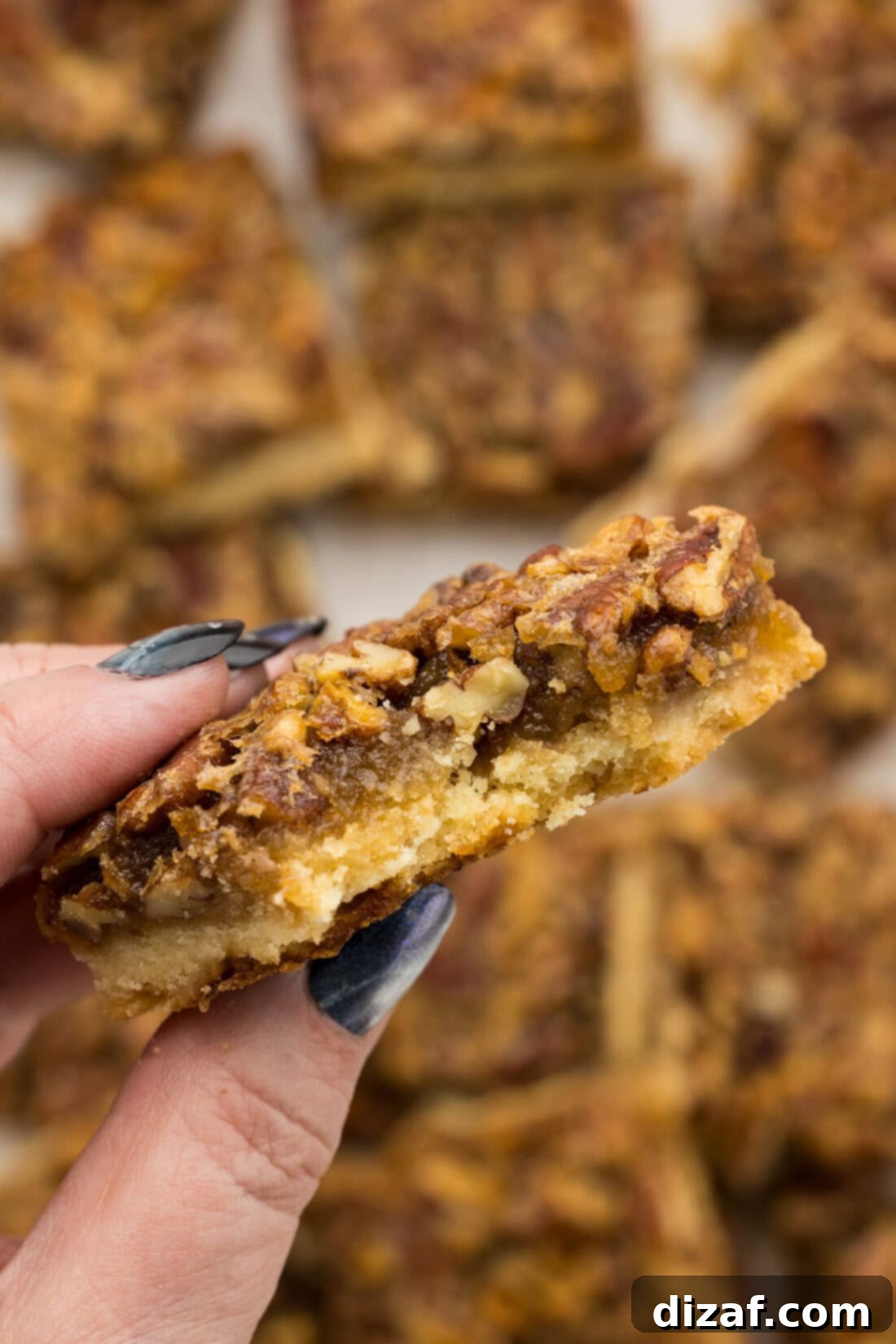 Hand holding a Pecan Pie Bar with a bite removed, showing the golden crust and rich filling