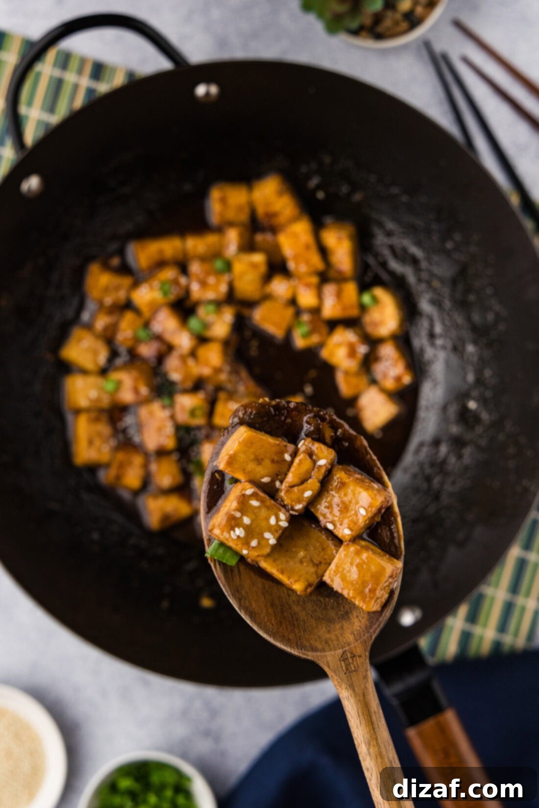 Savory Glazed Teriyaki Tofu 3 A spoonful of glossy Teriyaki Tofu held above a hot wok, showcasing the delicious sauce-coated pieces.