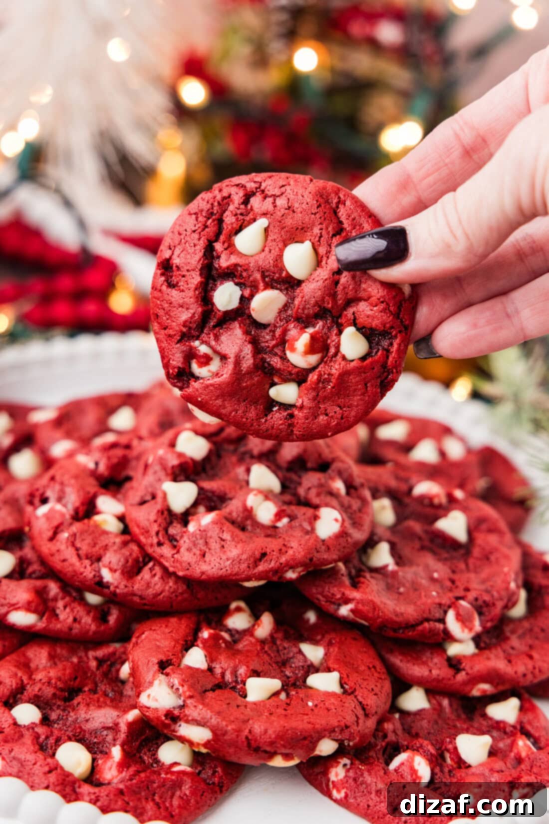 Hand holding a Red Velvet Cake Mix Cookie over a plate of more cookies