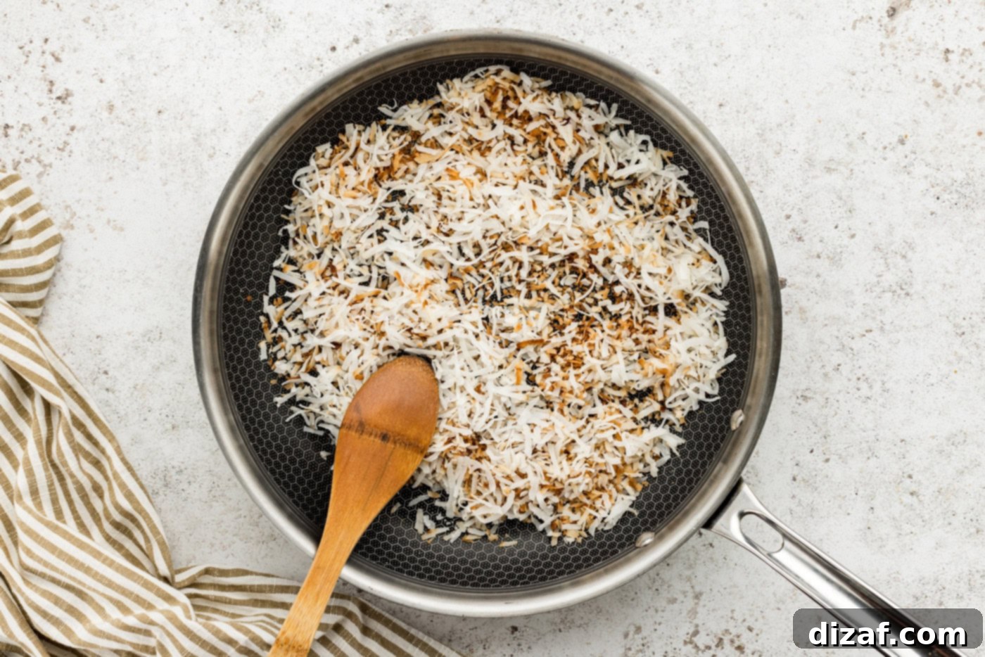 Toasted shredded coconut in a skillet with a wooden spoon