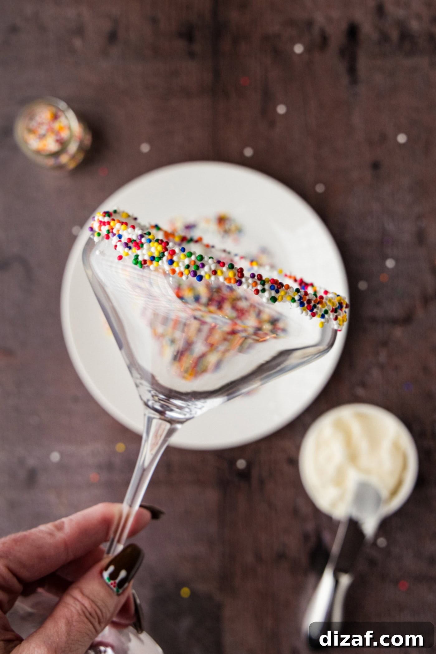 holding a martini glass with the rim coated in frosting and rolled in sprinkles