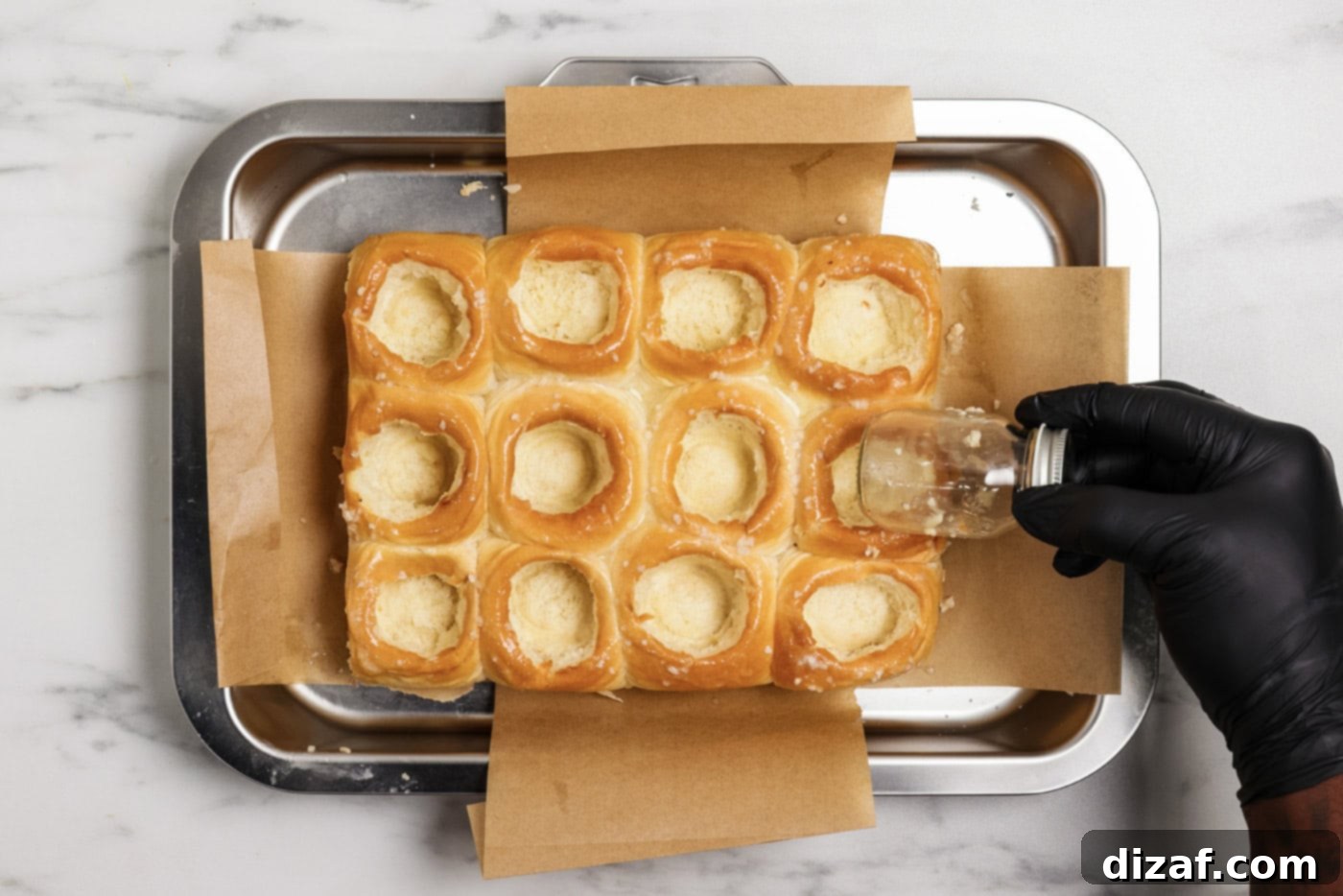 Hand using a mason jar to create even holes inside bread rolls, preparing them for the filling.