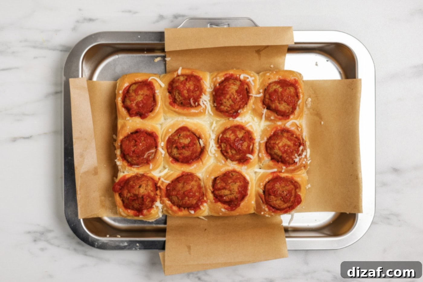 Meatball and marinara sauce being added on top of the cheese inside the dinner rolls.