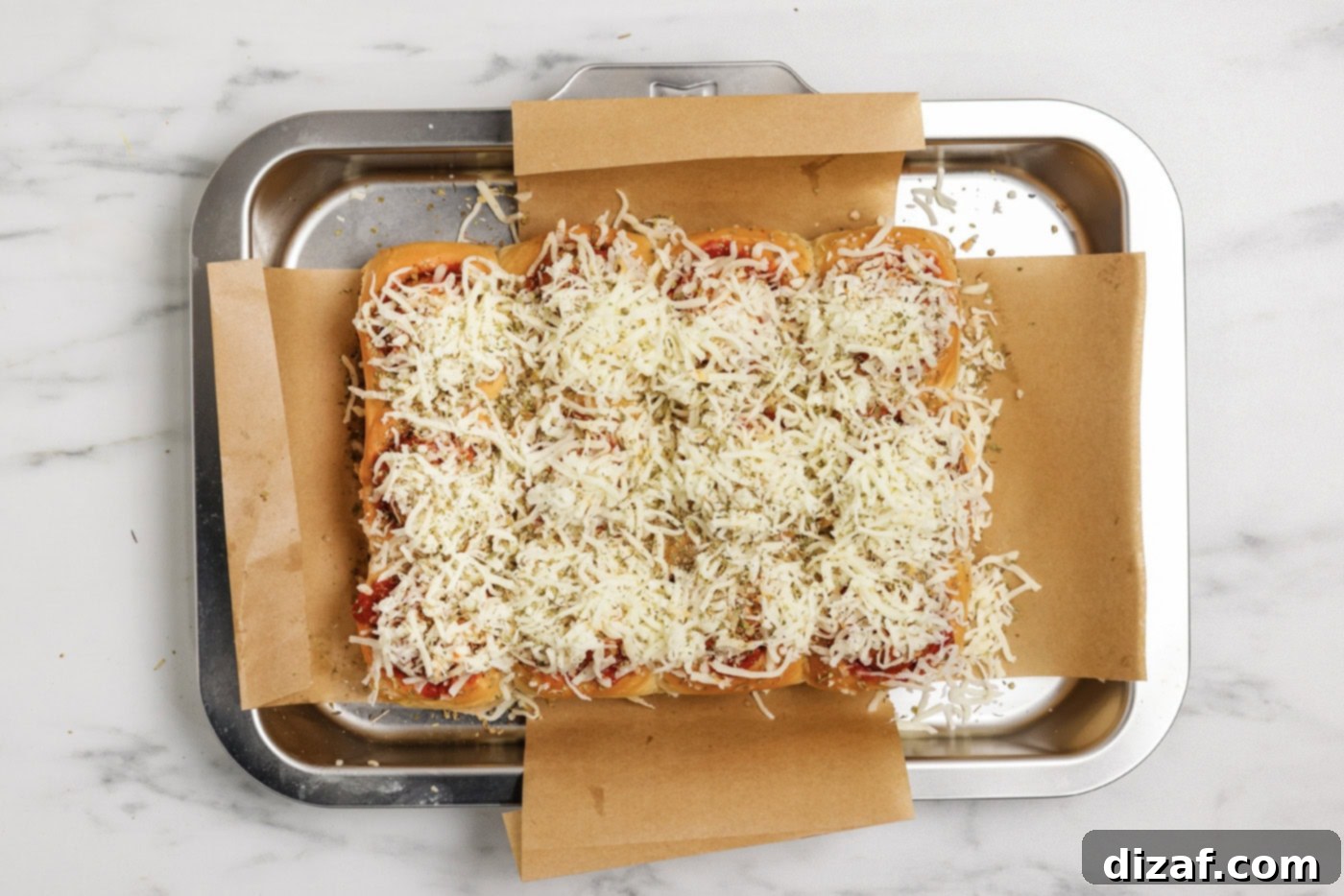 Shredded mozzarella cheese and parsley sprinkled on top of the meatball sliders before baking.