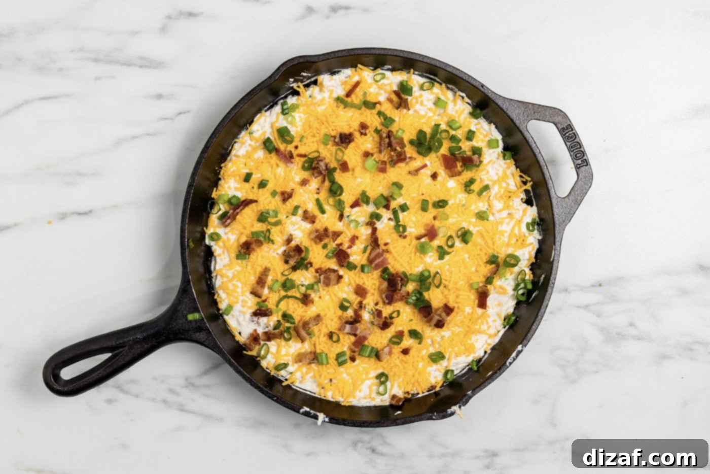 Dip covered with cheese, bacon, and onions in a skillet