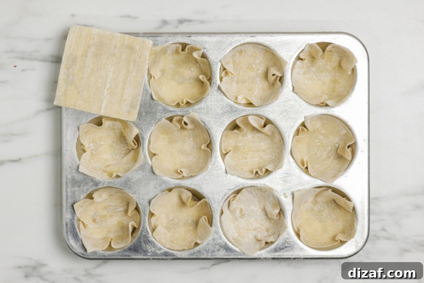 Wonton wrappers tucked inside muffin pan cavities