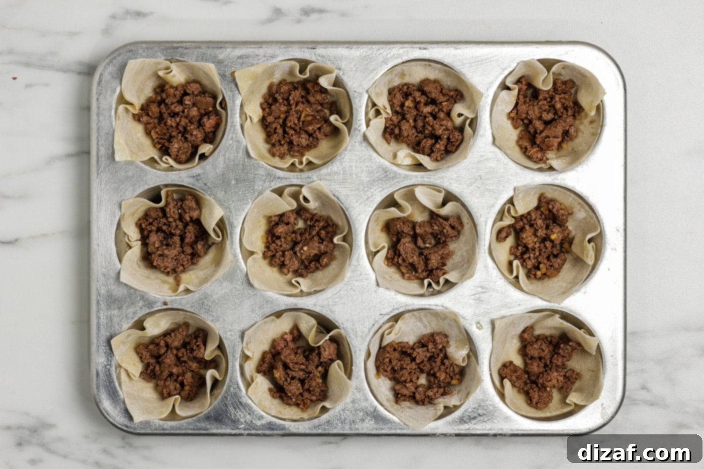 Taco meat placed inside wonton wrappers in a muffin pan