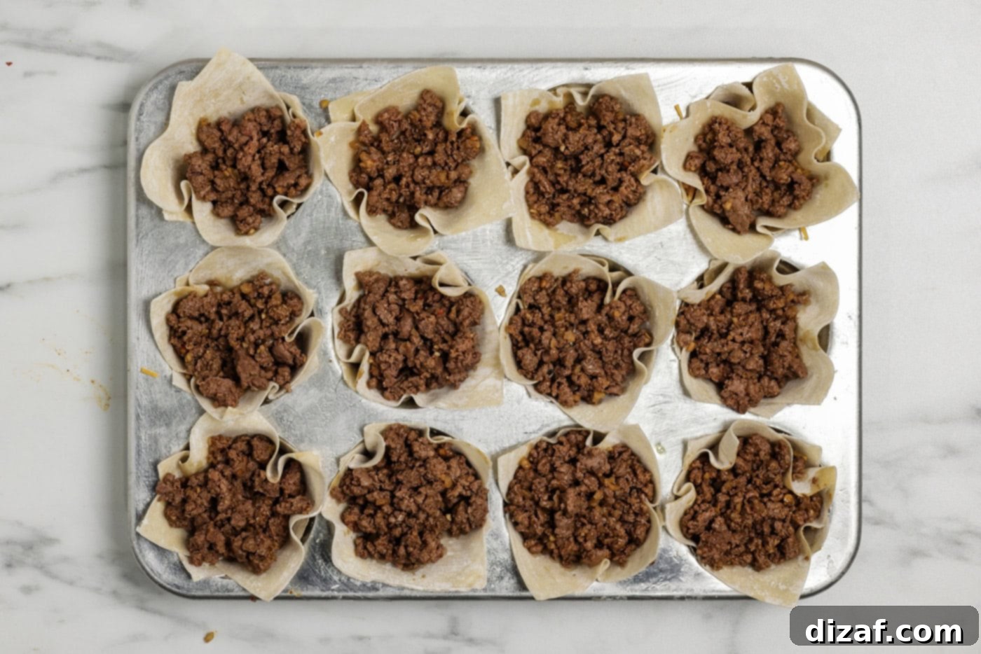 Taco meat layer overtop shredded cheese inside a wonton wrapper