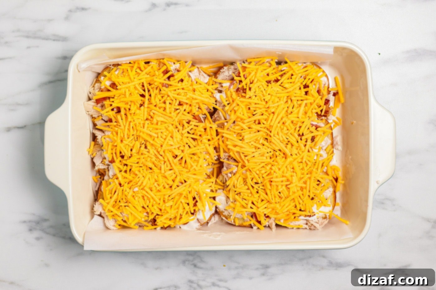 Shredded cheese over chicken, bacon, and ranch sliders in baking dish