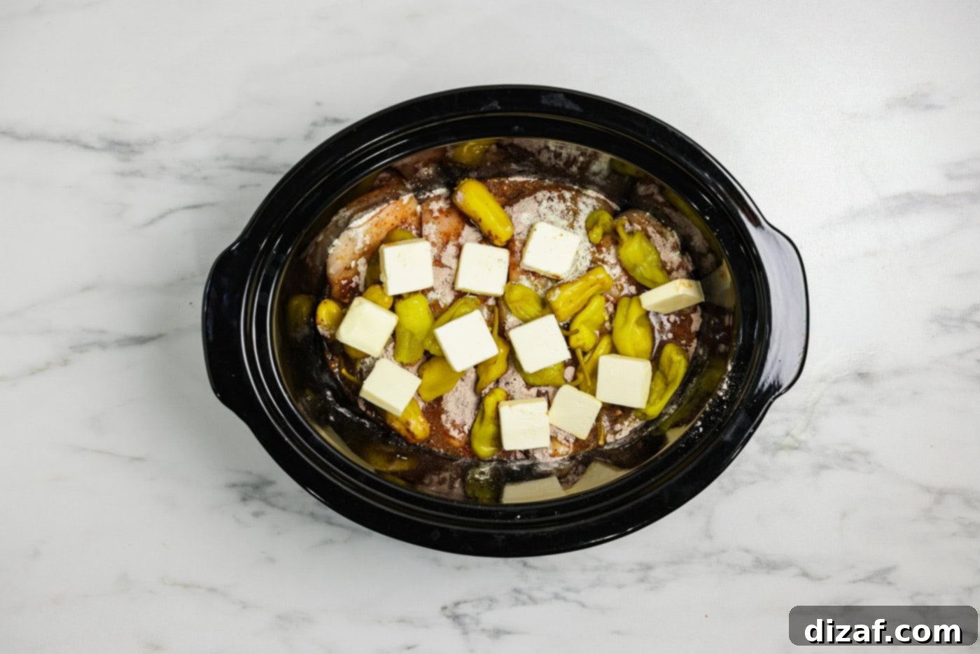 Butter pats on top of pepperoncinis, ranch seasoning, Au jus packet, and chicken breasts in a crock pot